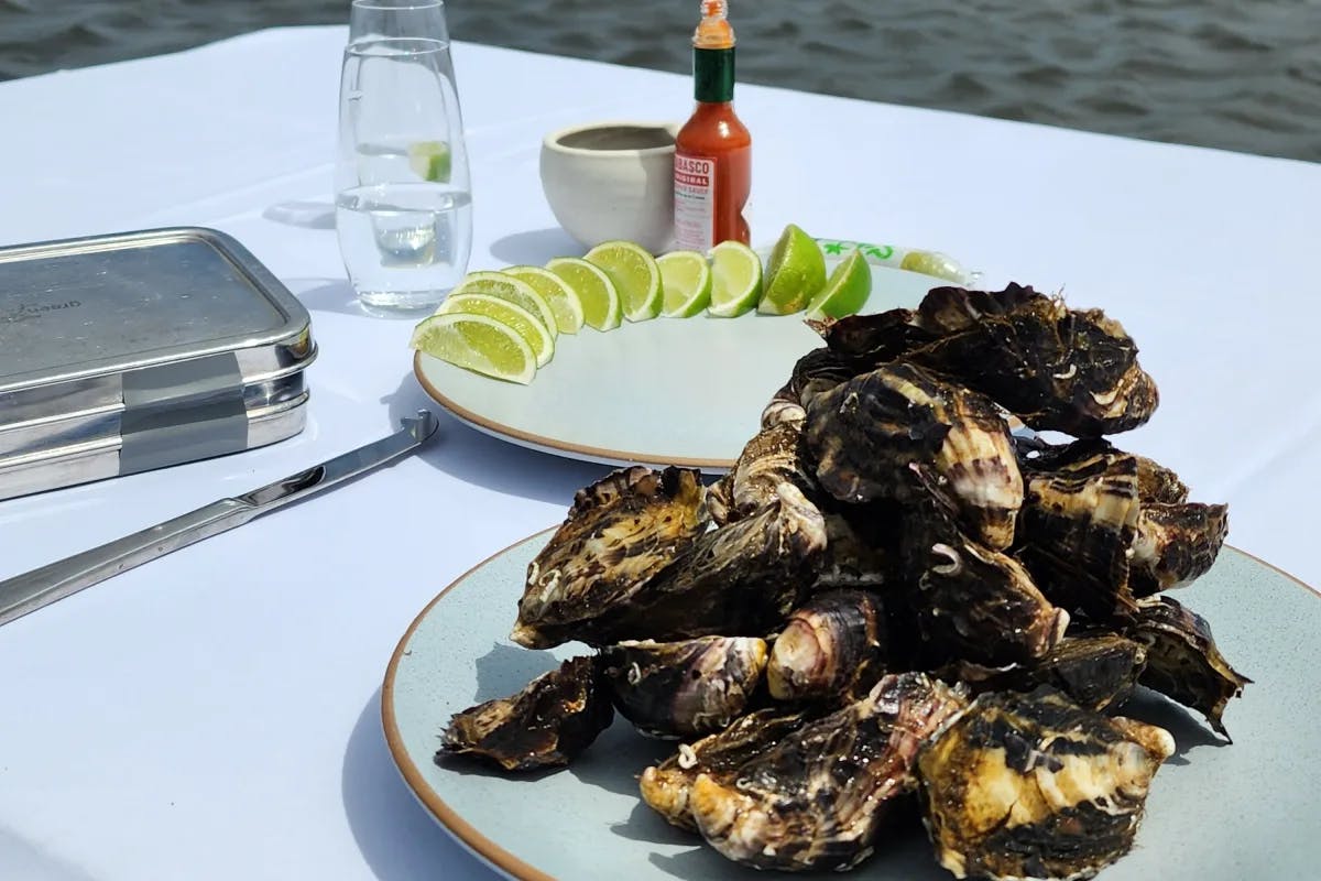 A white table with a plate of oysters and another plate of limes on a body of water.