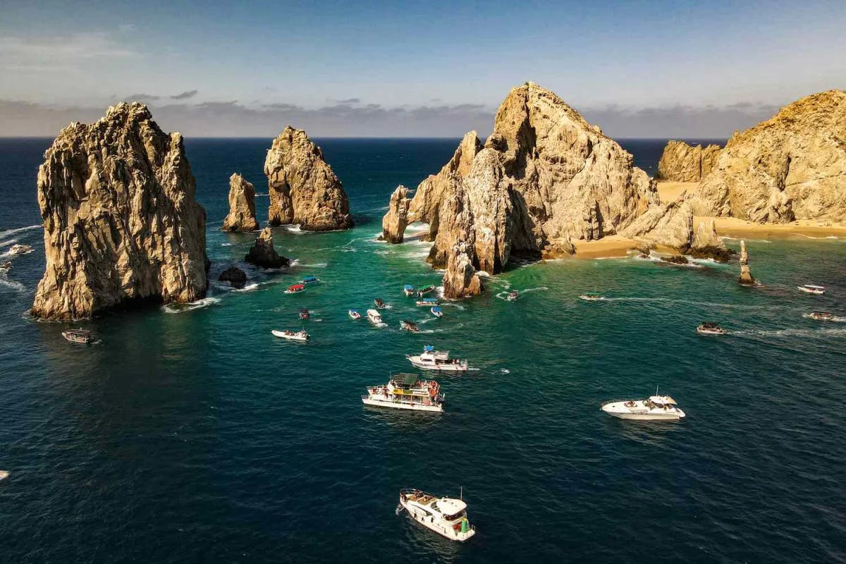 Aerial view of boats in the ocean by rock formations in Cabo