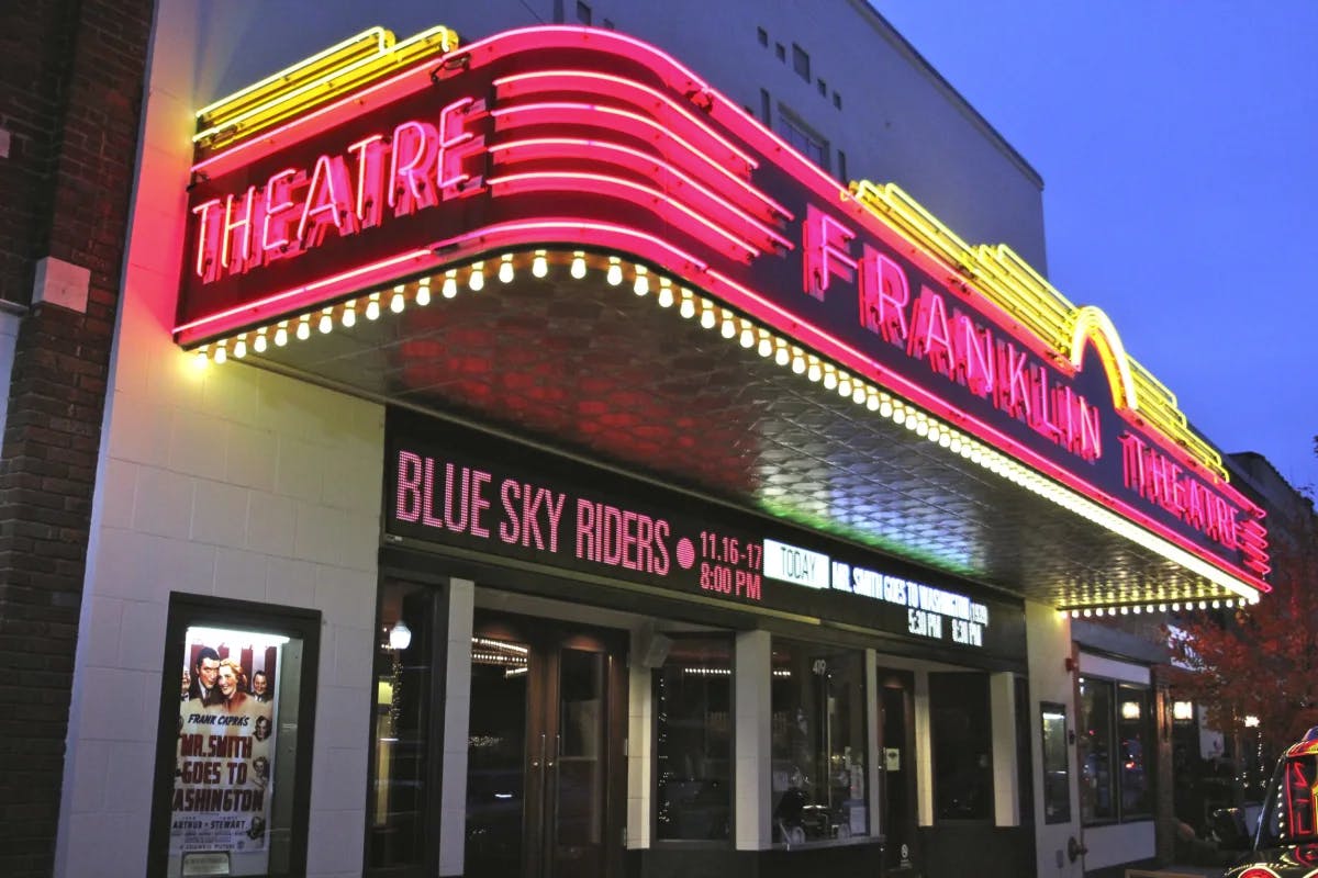 The exterior of Franklin Theatre lit up in neon lights at night.