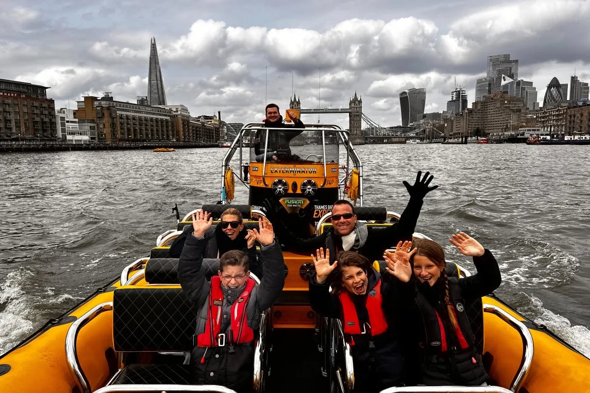 A family posing with their hands in the air on a yellow speed boat in the River Thames with iconic London skyline in view.