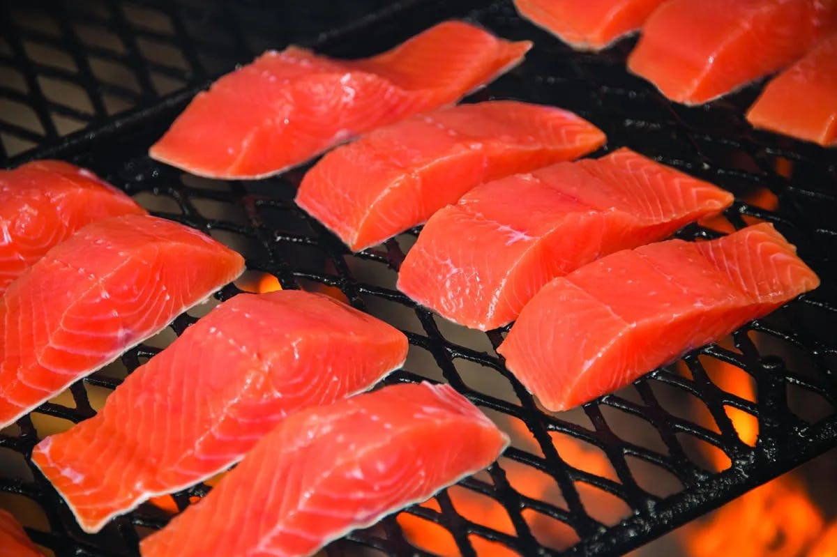 A picture of rows of red-colored salmon fillets on a grill