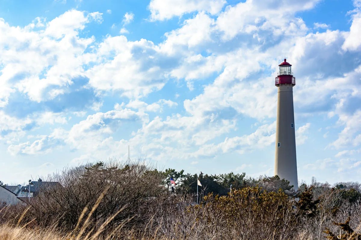 The red and white Cape May lighthouse in a field of brush with blue sky and clouds.