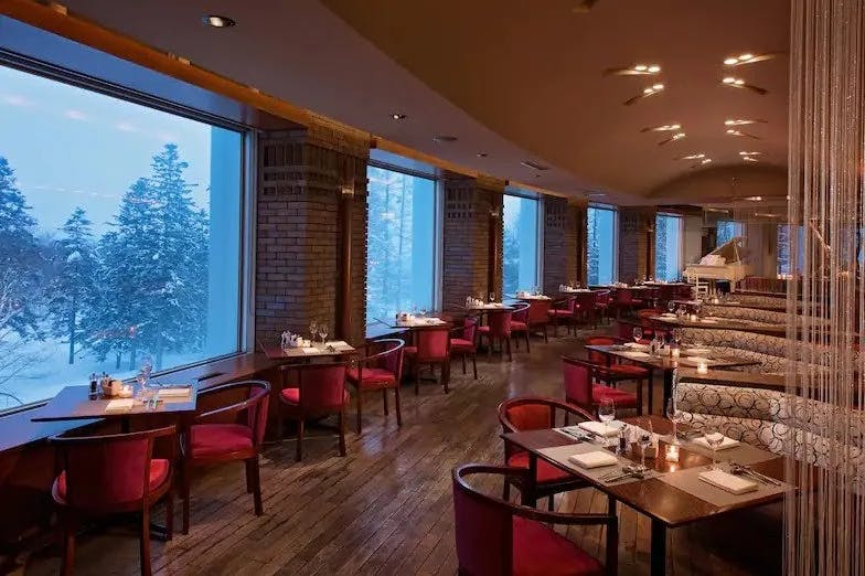 Dining area of Melt Bar and Grill at Niseko Village with red chairs and large windows looking out to the snowy landscape