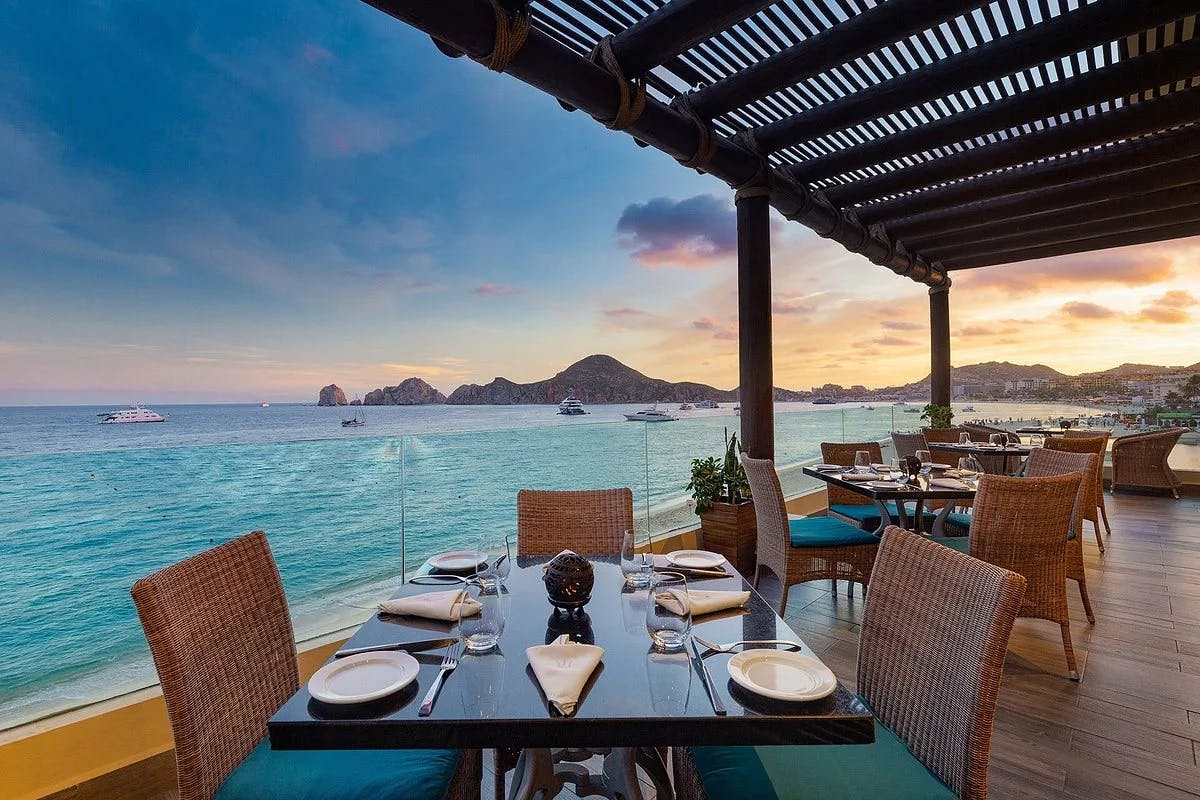 An outdoor restaurant with brown wicker chairs with ocean views in Cabo