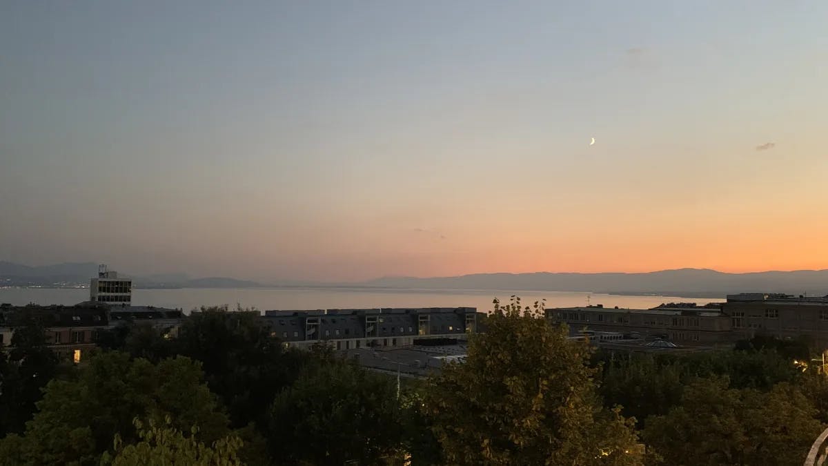 Lake Geneva at sunset. There is a strip of land and a moon crescent in the distance. 