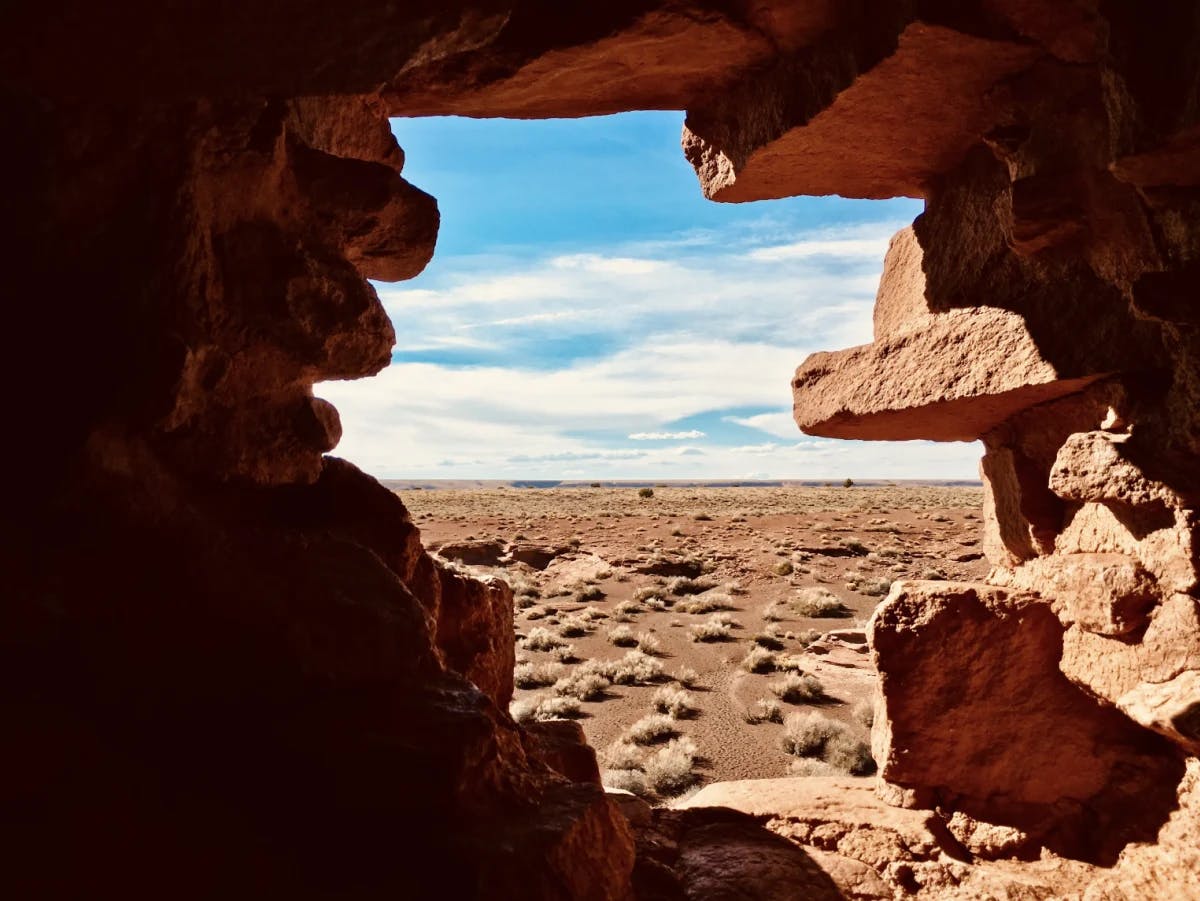 A view of red, rocky and desert-like terrain from an opening of a rocky cave. 