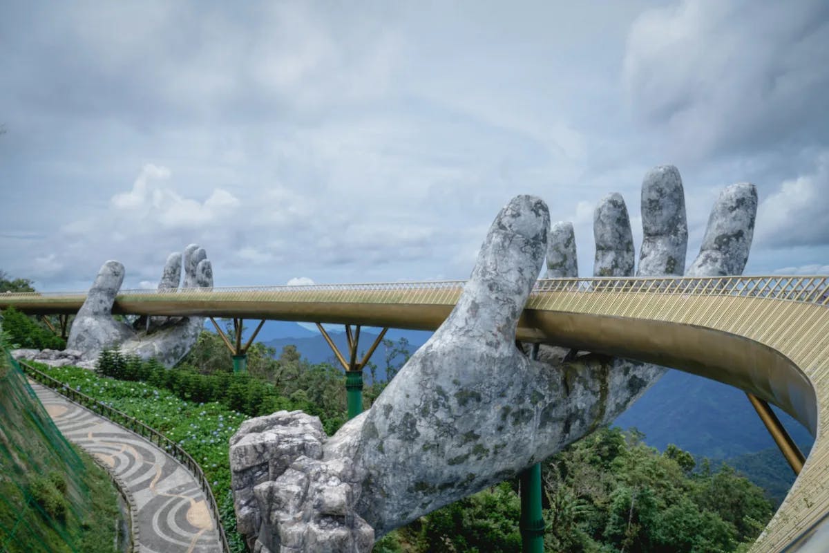 A view of the famous Golden Bridge with large stone hand structures and golden railings