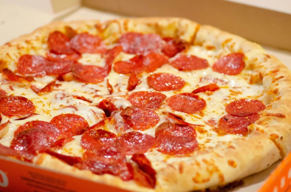 A pepperoni pizza in a box cut into slices. 