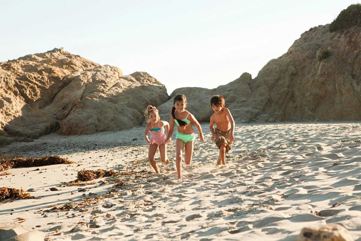 A picture of three children running on the beach during the daytime.