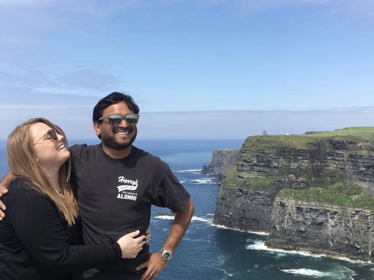 A couple posing in front of a view of cliffs on the water during the daytime