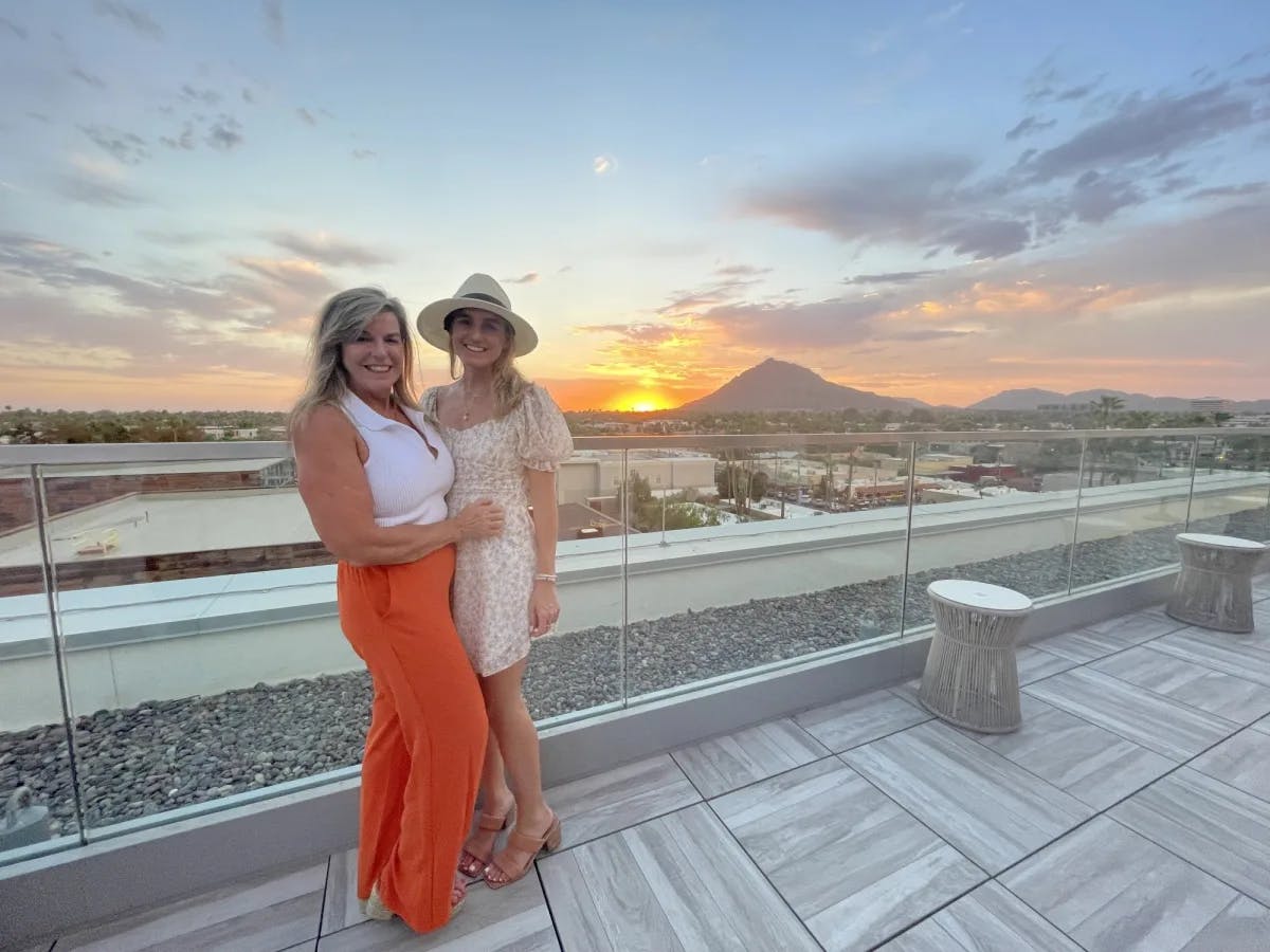 Two women on a balcony with a sunset in the background.