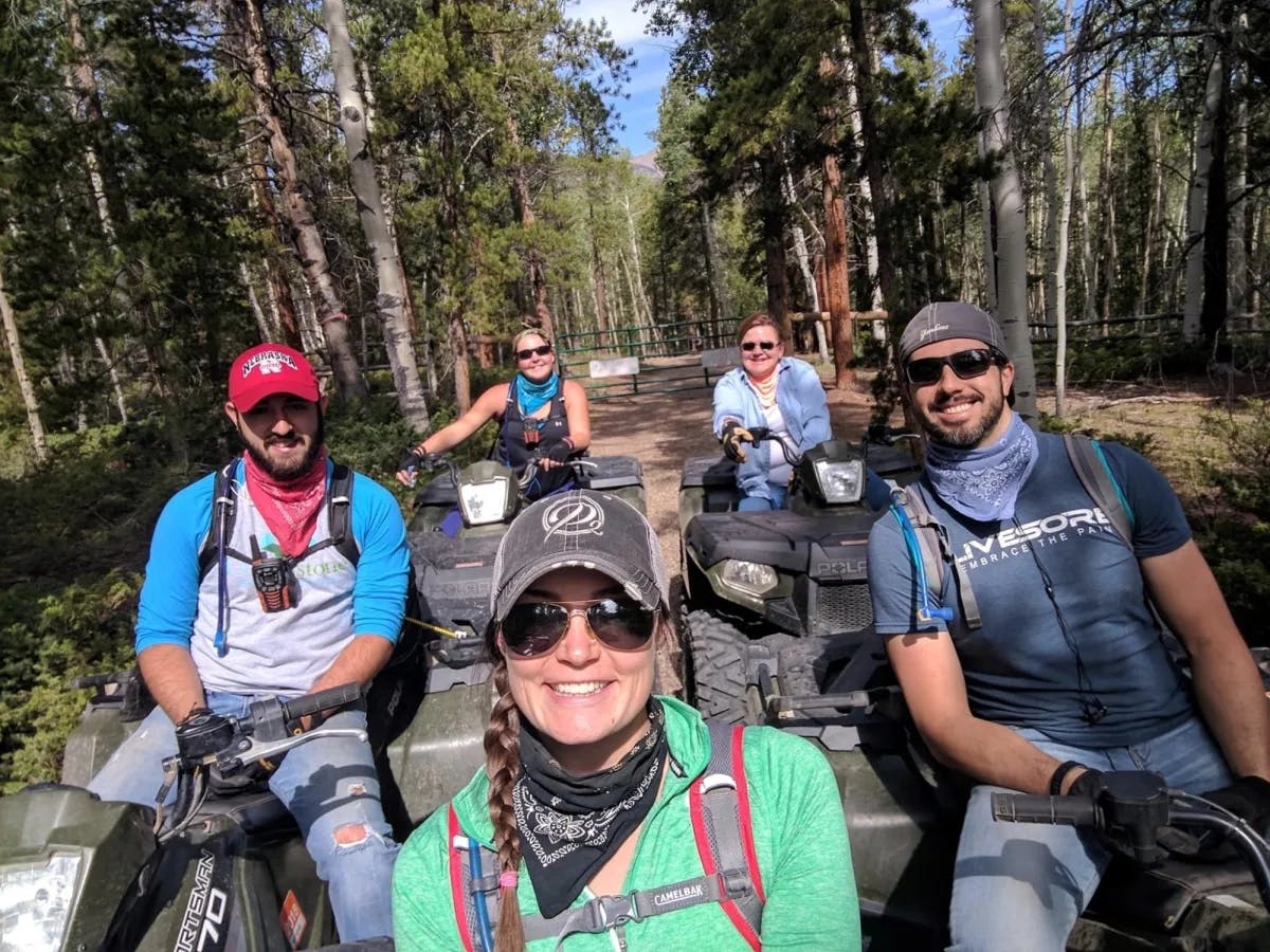 A group of people riding ATVs on a path through a forest with tall trees