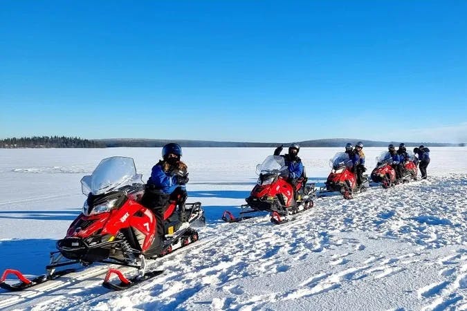A group of people sitting on red snowmobiles in a snowy field on a clear day.