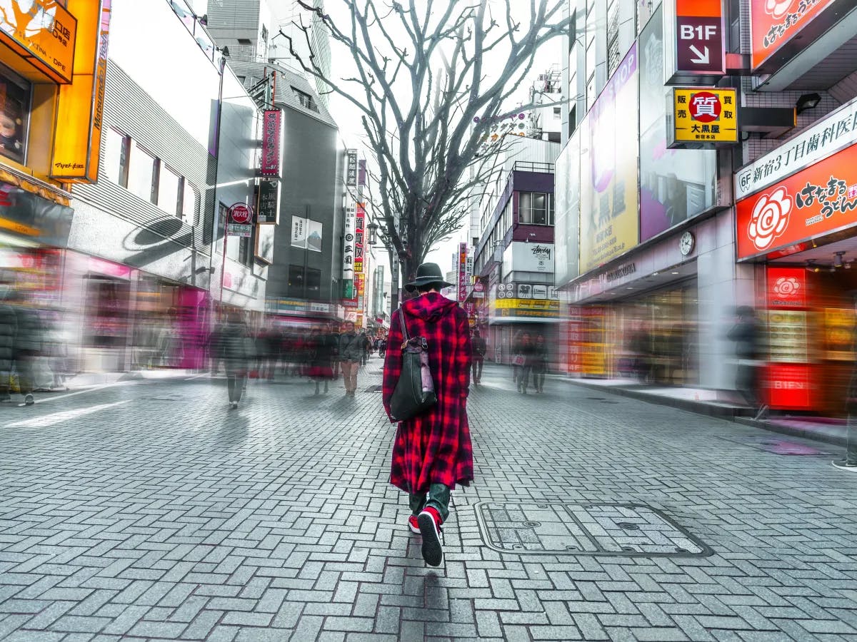 A selective focus photography of a person in a red plaid jacket walking on the streets during the daytime.