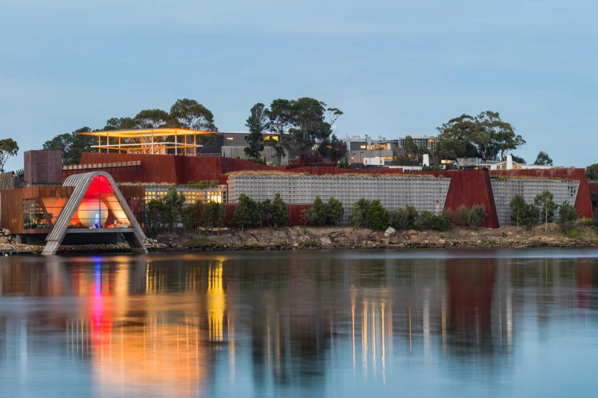 A lit up MONA - Museum of Old and New Art - beside the River Derwent at twilight.