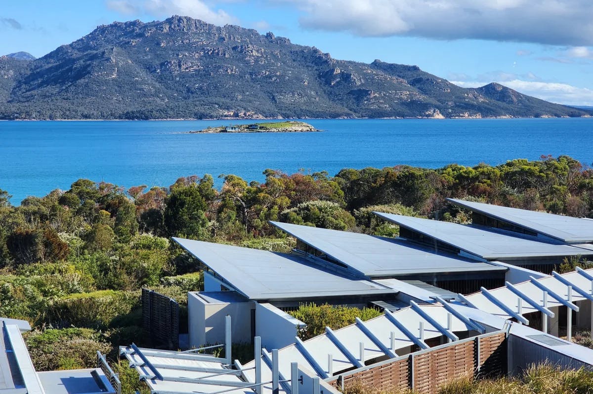 A view from the Saffire Freycinet, with solar panels in the foreground and green trees beside a blue body of water with mountains in the background.