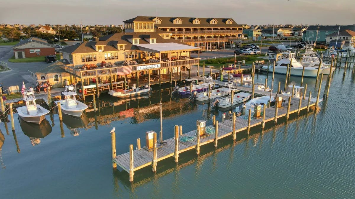 An aerial view of a boardwalk with docked boats, buildings and a small town in the background. 