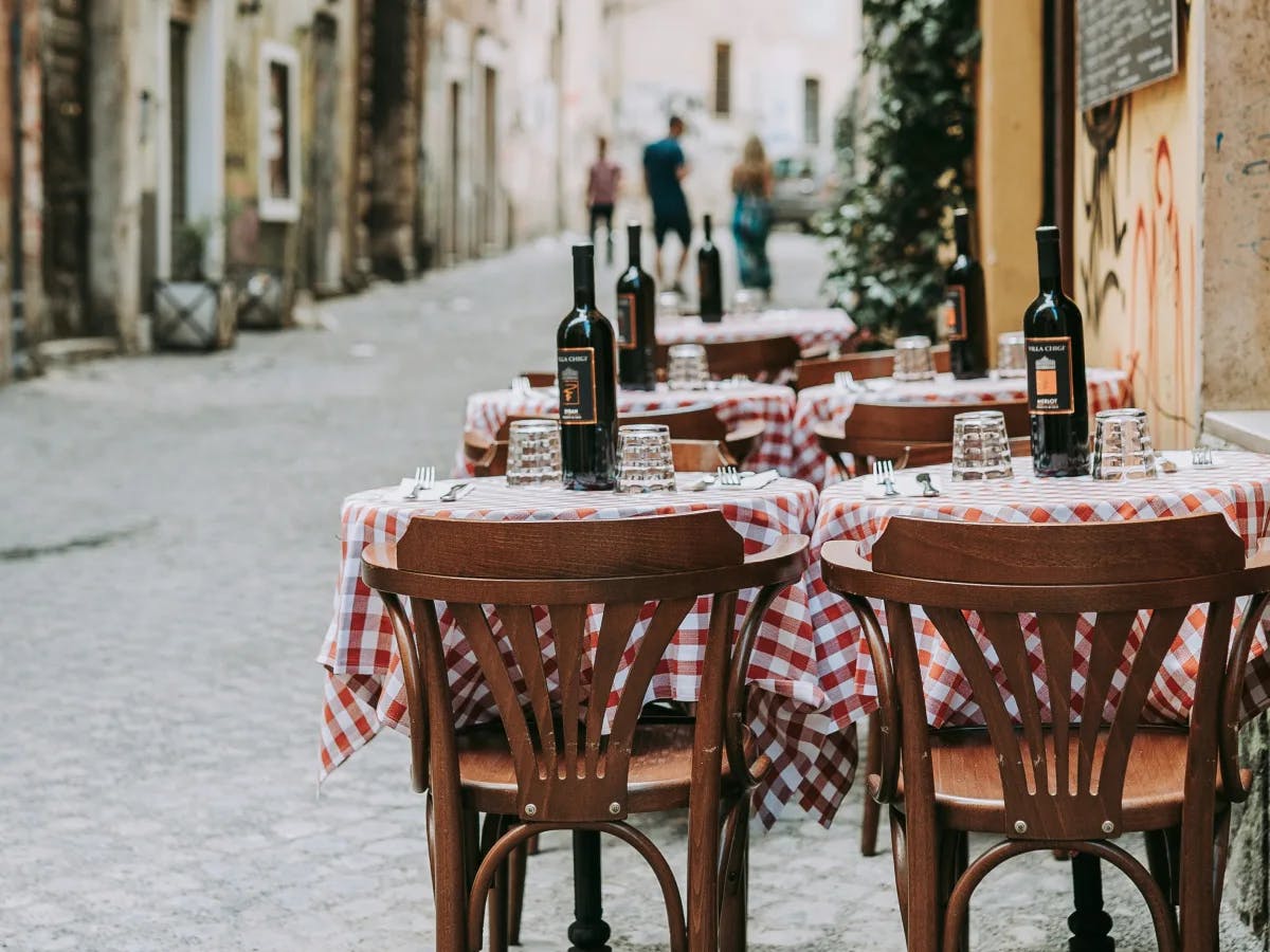 An Italian outdoor restaurant with wooden chairs and a bottle of wine on the table during daytime.