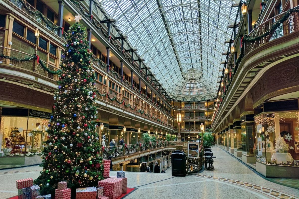 A view of the mall at Christmas time with a tree, glass ceiling, balconies and retail stores lining both sides. 