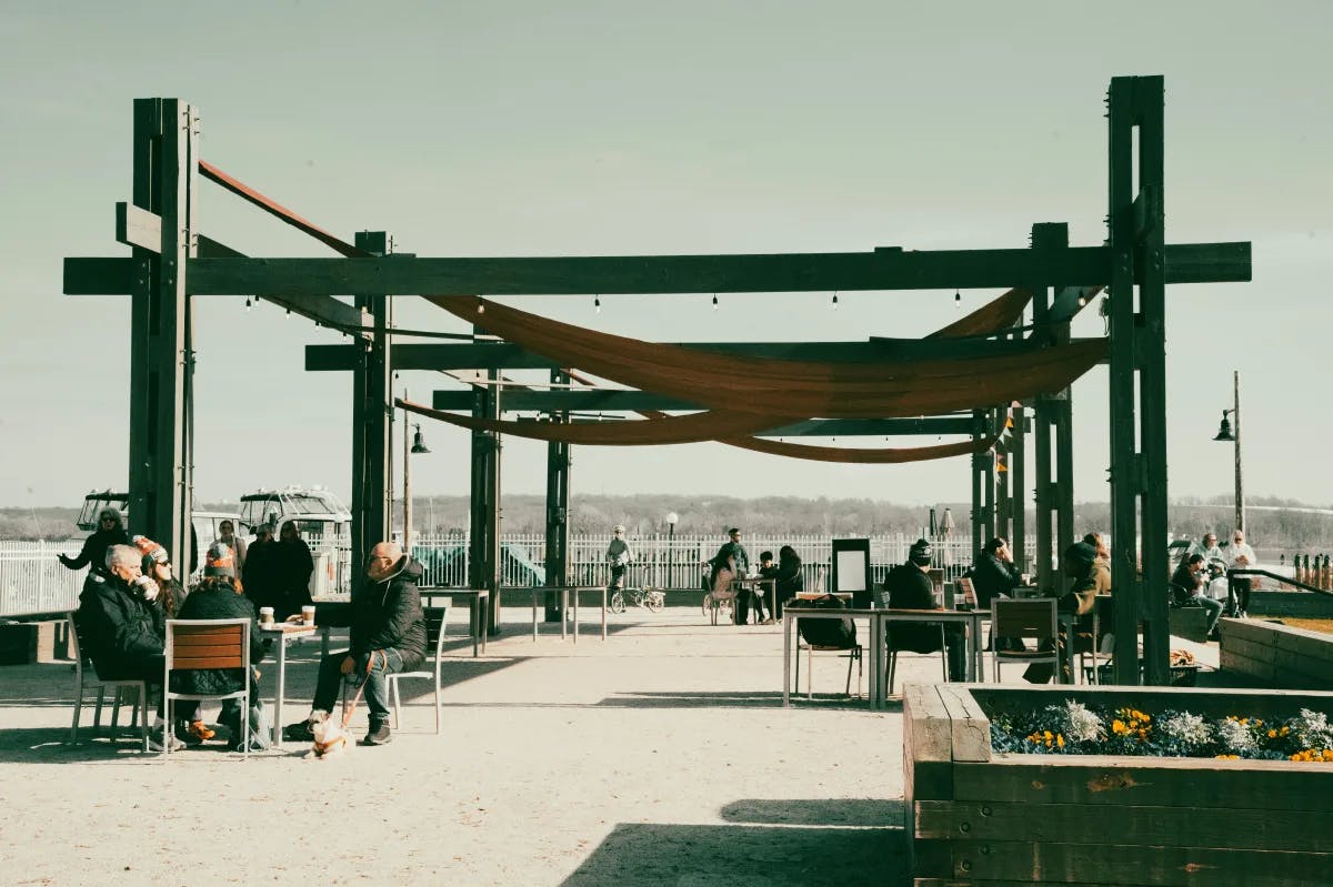 A group of people sitting on a waterfront patio drinking coffee under beams.