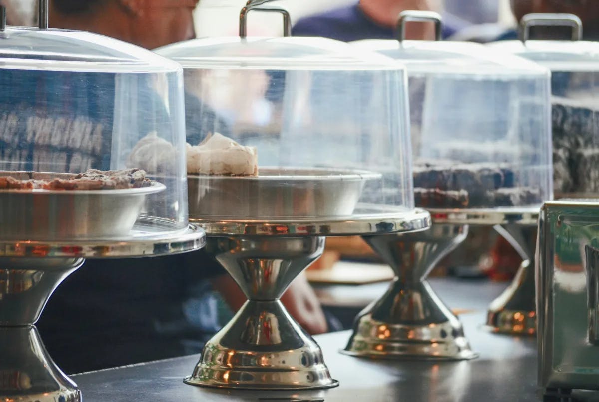 A row of cake stands full of various pies in platters covered by a clear lid. 