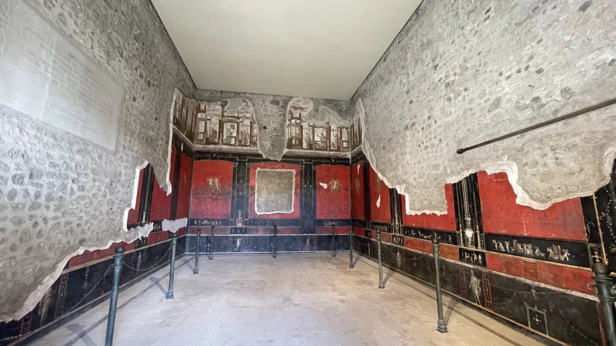 An interior with stone and old wallpaper that is red with black detailing. 