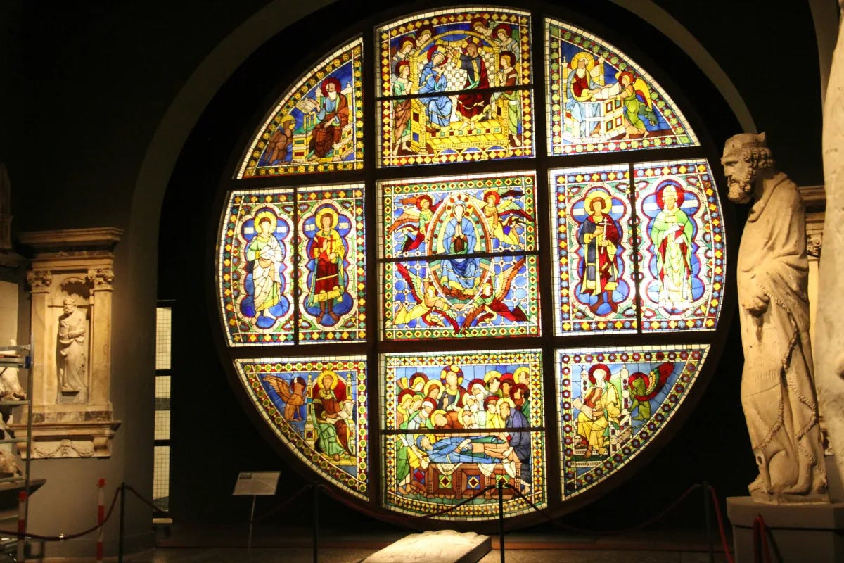 A colorful stained glass window inside a cathedral with statues on either side.