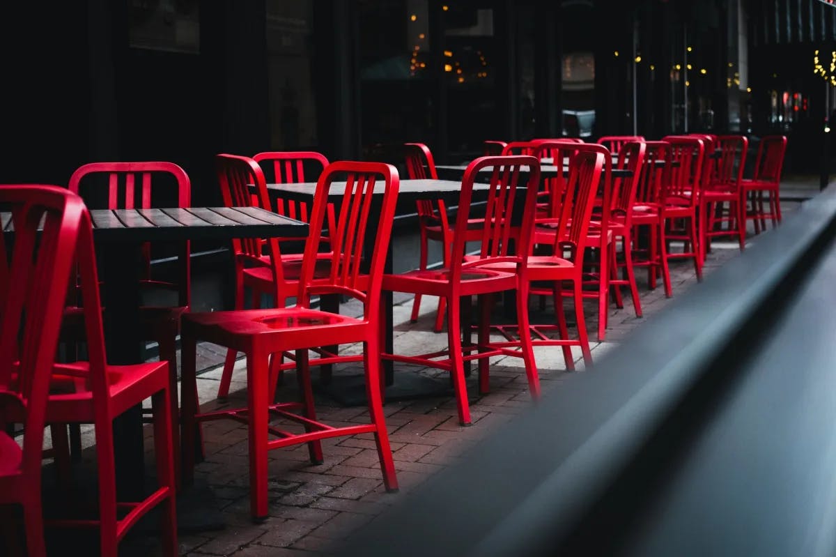Outdoor patio of a restaurant with red chairs and black tables.