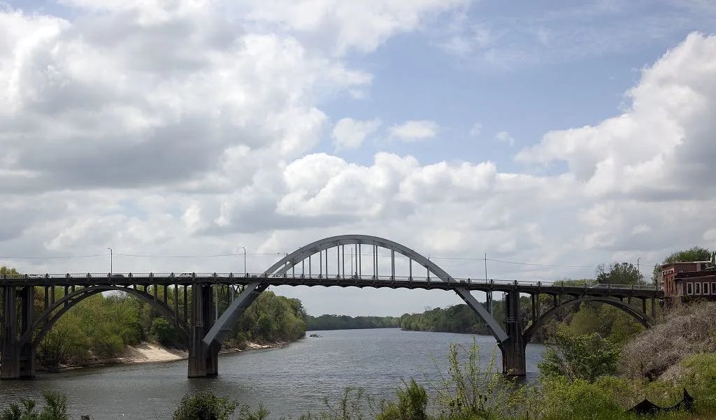 The Edmund Pettus Bridge from a distance over a river with greenery on either side.