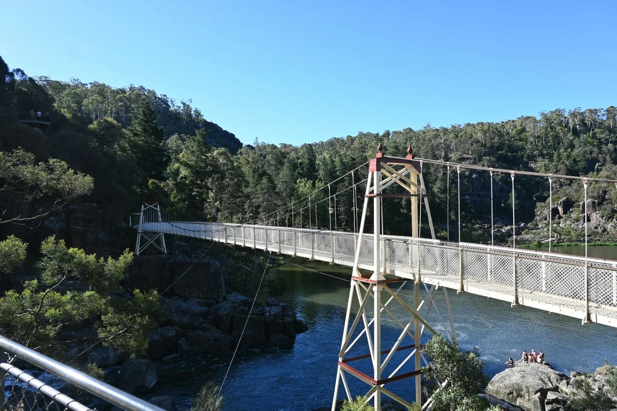 Alexandra Suspension Bridge in Cataract Gorge Reserve, a long bridge over water leading to green tree-covered hills.