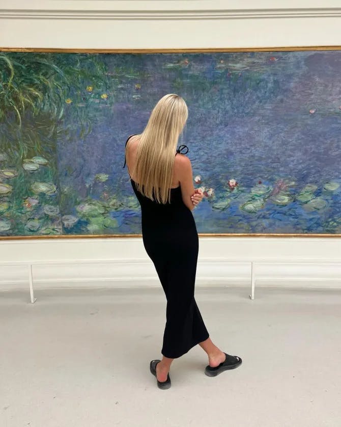 Travel advisor Olga in a black dress admiring a blue and green painting at a gallery