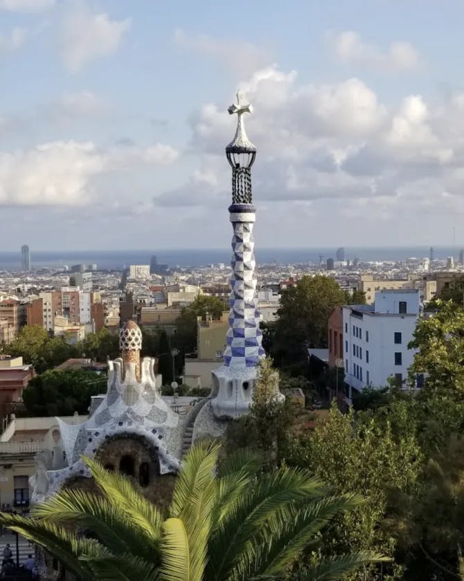 A blue and white spiral in front of a city view in the distance. There are trees and bushes in the forefront. 