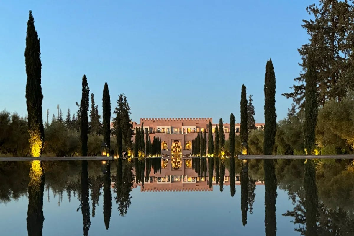 a long pool flanked by cypress trees leads up to a regal palace