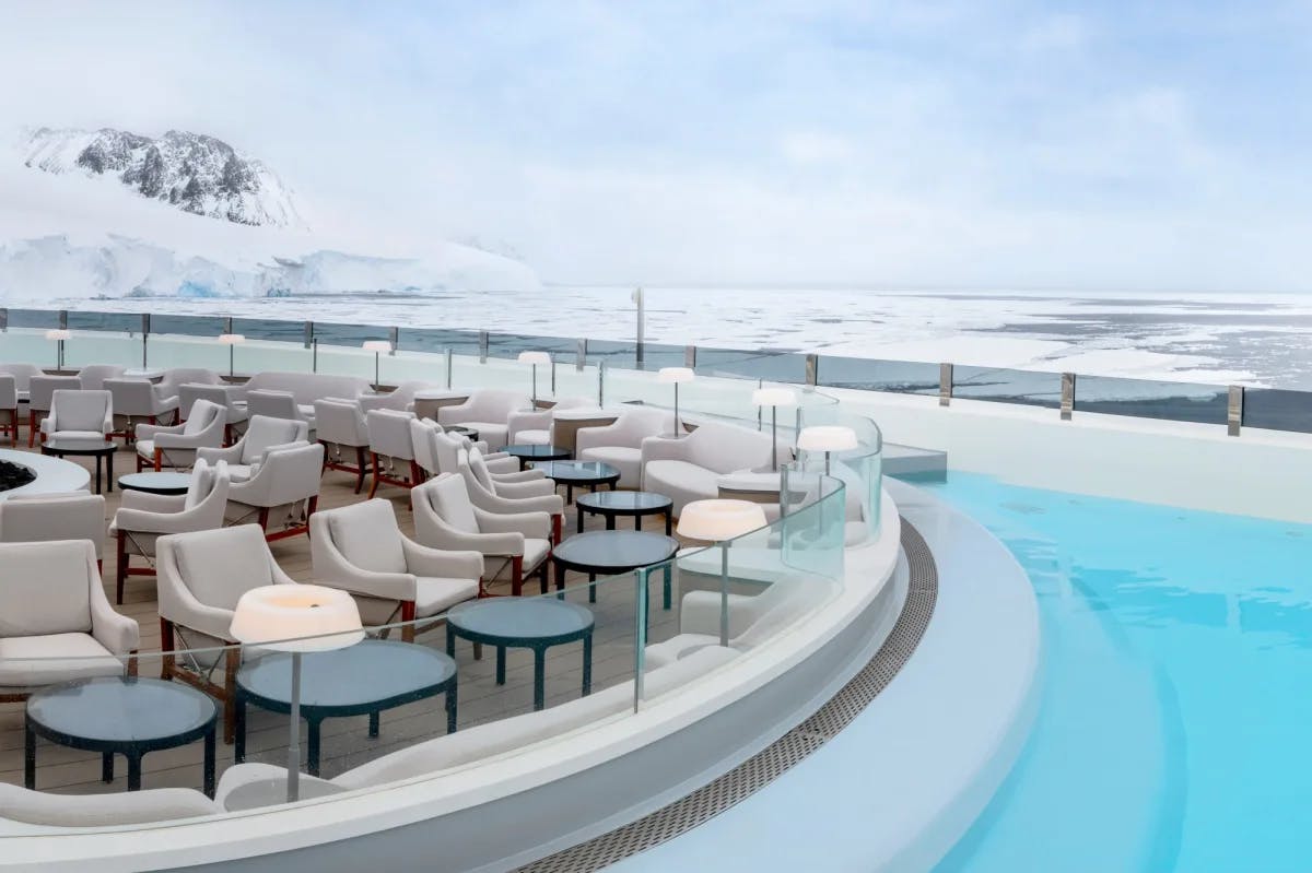 a cruise ship deck dotted with chairs and tables overlooking a pool amid a snow landscape