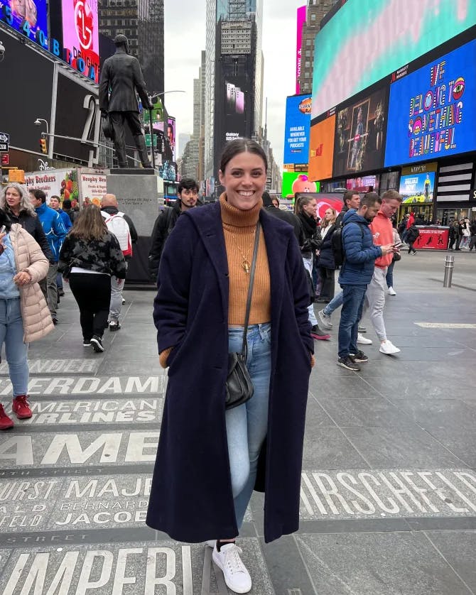 Travel advisor Brittanie posing for a photo in a navy coat and orange sweater in Times Square