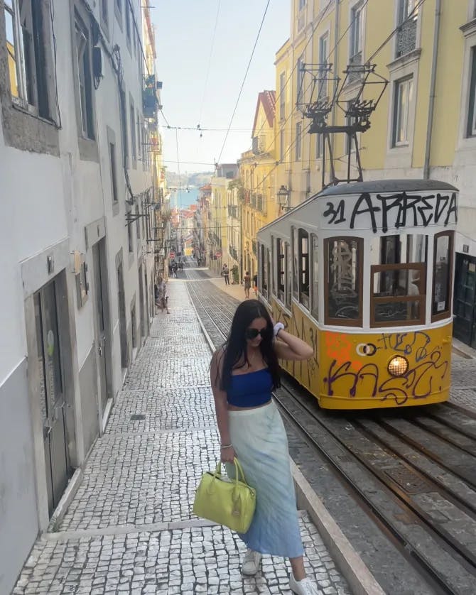 Picture of Ashley walking along along a narrow street with an old yellow and white tram car passing her by. 