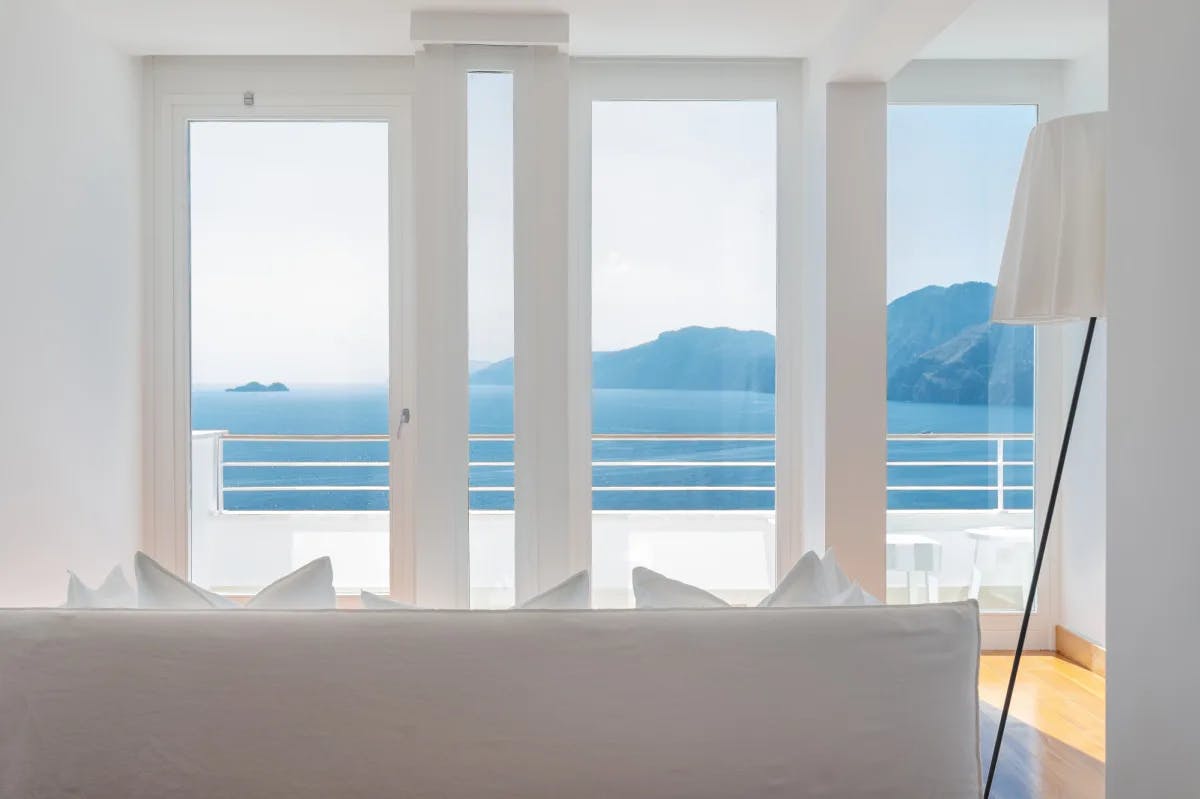 a white couch overlooks the sea through white-rimmed doors