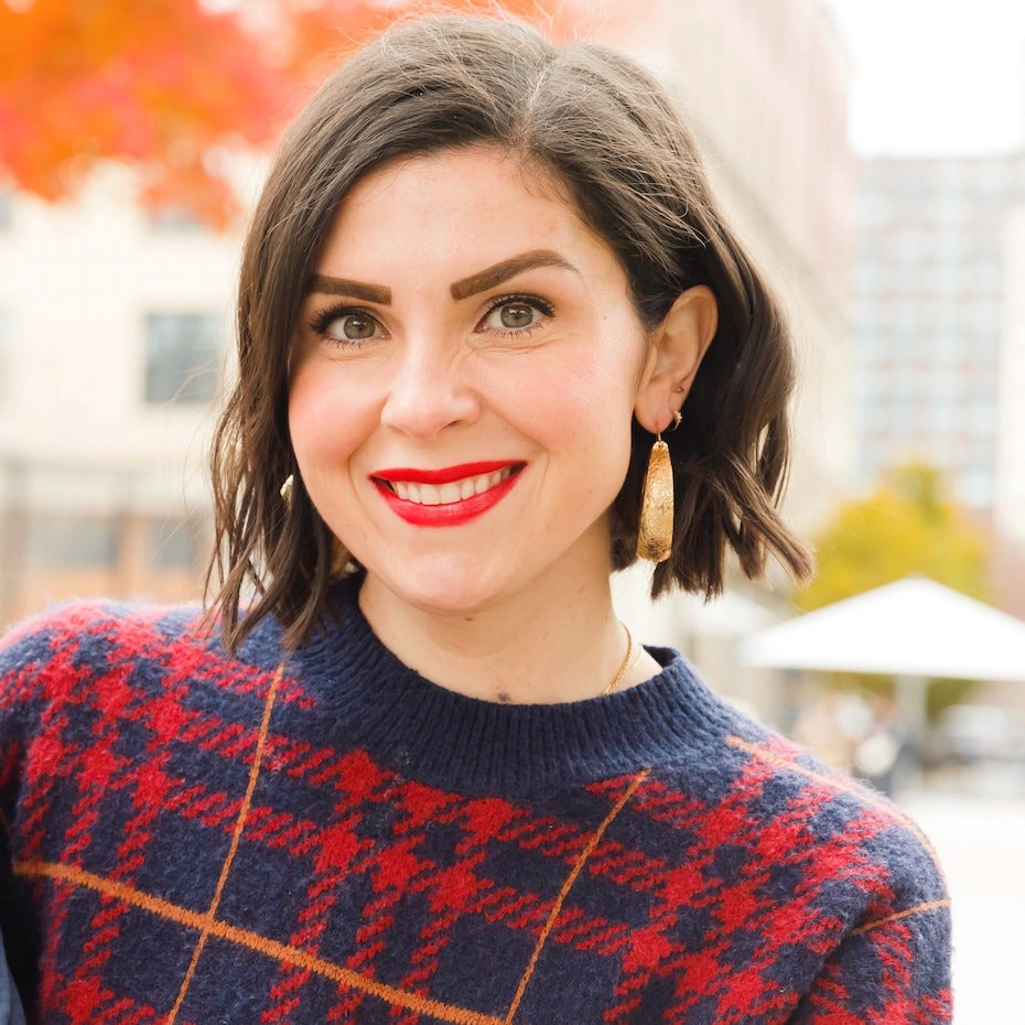 Lindsay wearing a red, orange and navy blue checkered top with gold earrings while posing outside