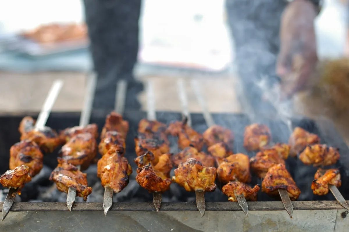 Chicken brochettes cooking over a lit charcoal grill