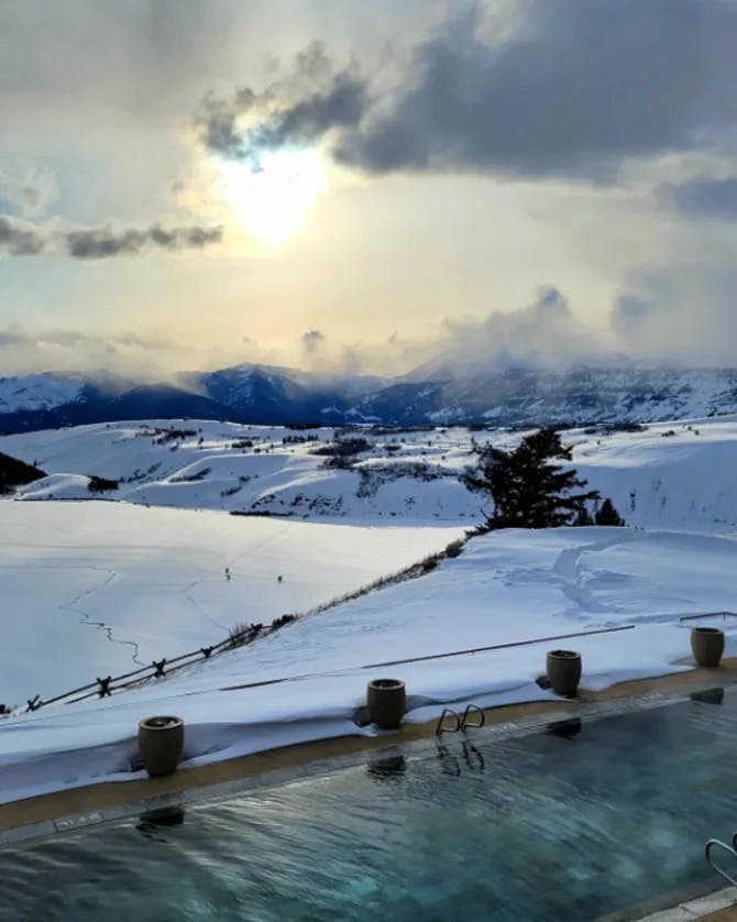 An infinity pool overlooking a snowy valley on an overcast day.