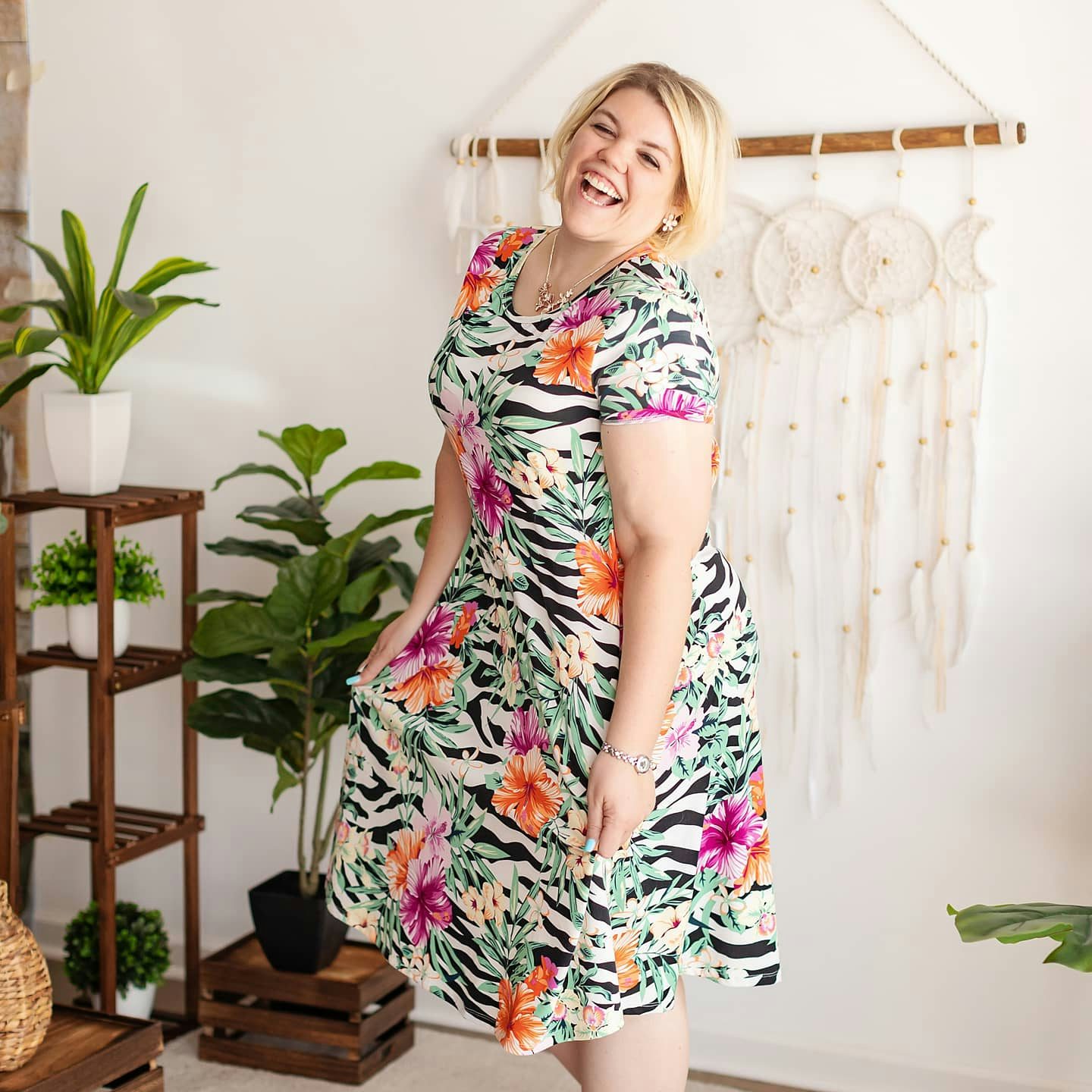 Erin Pifer posing for a photo in a colorful dress in front of plants and wall decoration