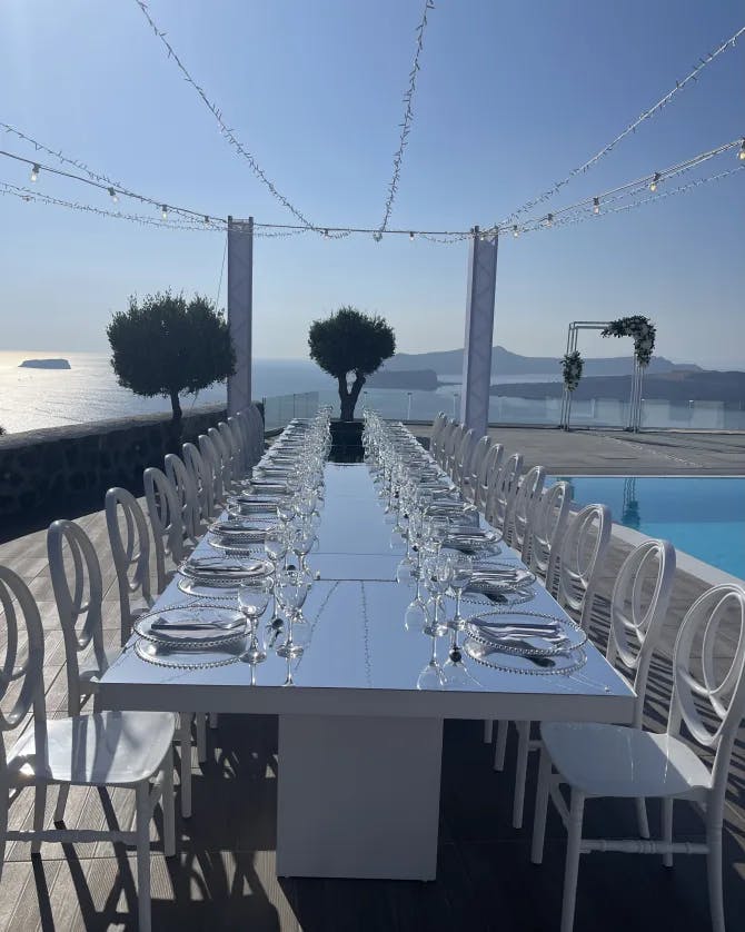 A long, elegant table set up on a pool deck overlooking the sea with string lights overhead.