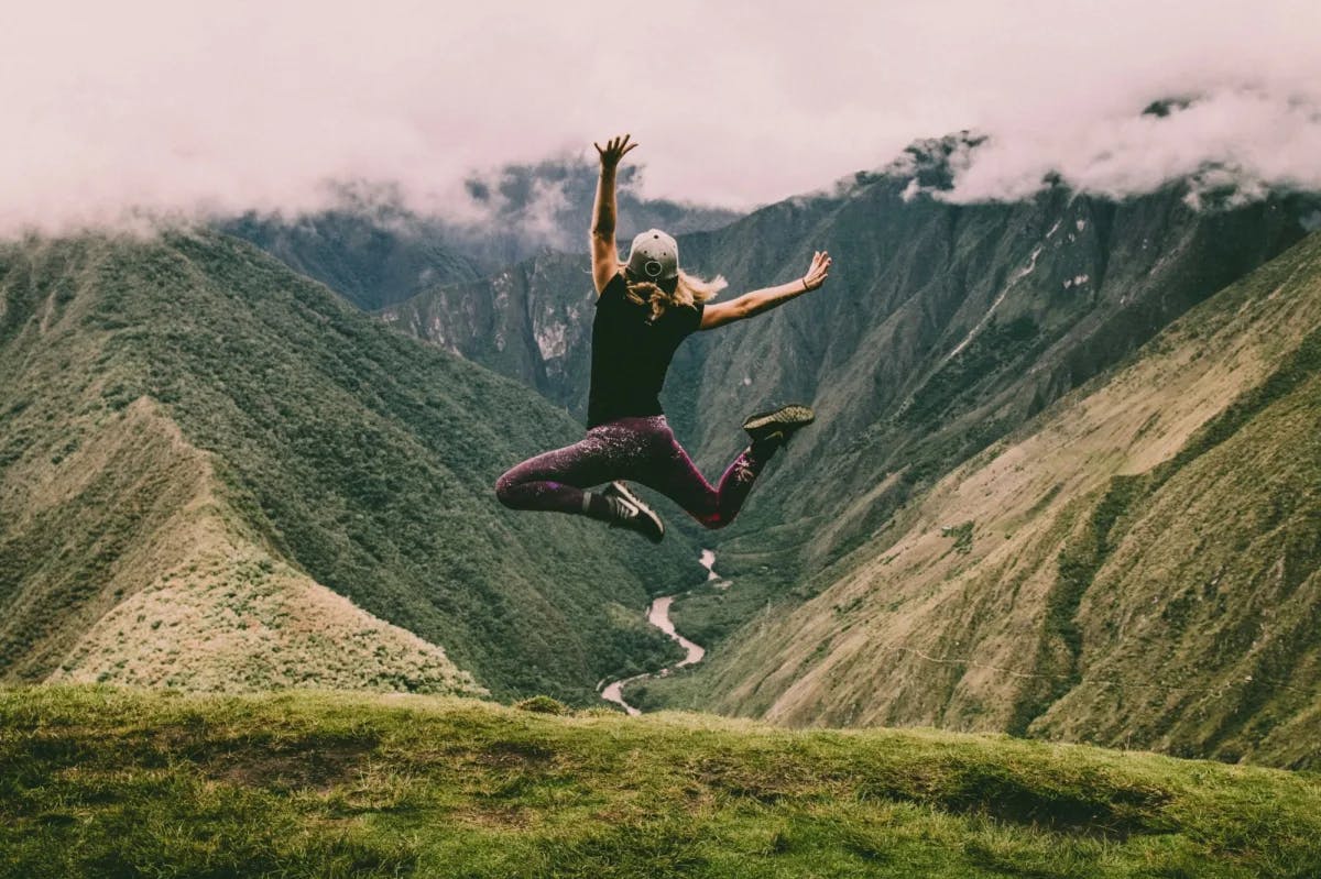 A young woman in the middle of a ecstatic jump for joy as she views the gorgeous Inca Trail in Peru