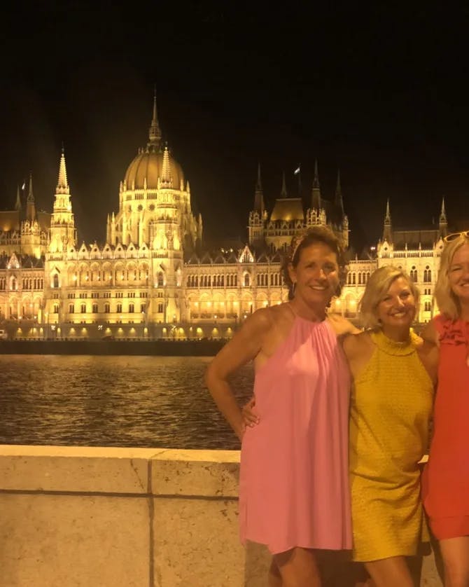 Travel advisor Kristin Rotter and three female companions posing for a group photo in Budapest in front of the river with lit-up building in the background