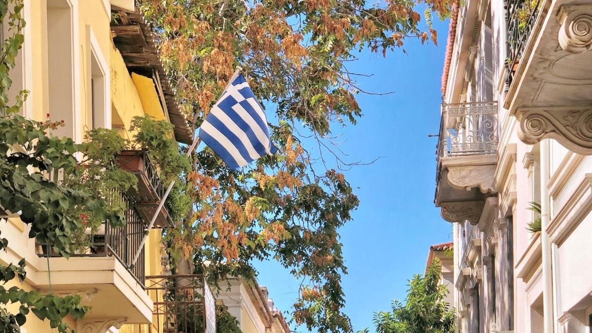 Sunny Athens backstreet with colorful townhouses, one of which is waving the Greek flag. 