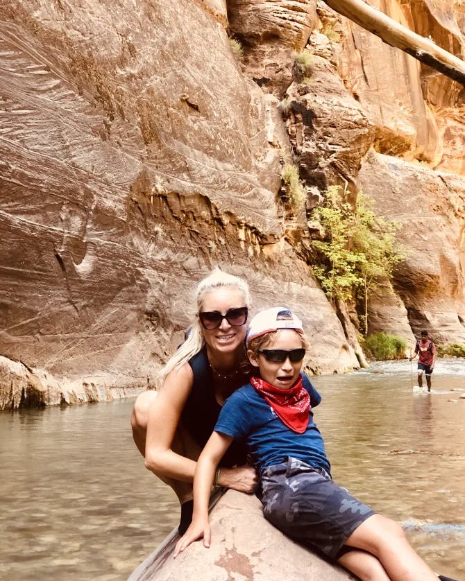 Travel advisor Elaine with child sitting on stone in body of water and large rock wall behind