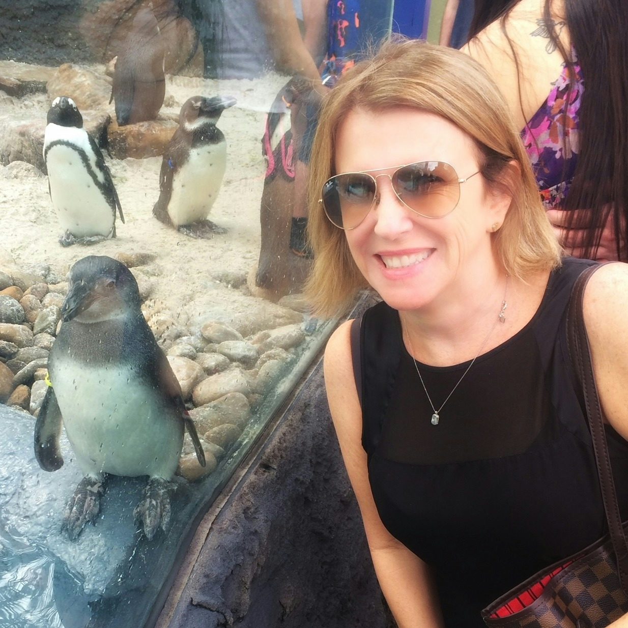 Carole Moore in a black top and sunglasses posing with penguins