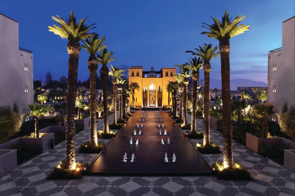 At twilight: a series of ornate fountains surrounded by palms and Moroccan-tile sidewalks lead to the main building at Four Seasons Resort Marrakech