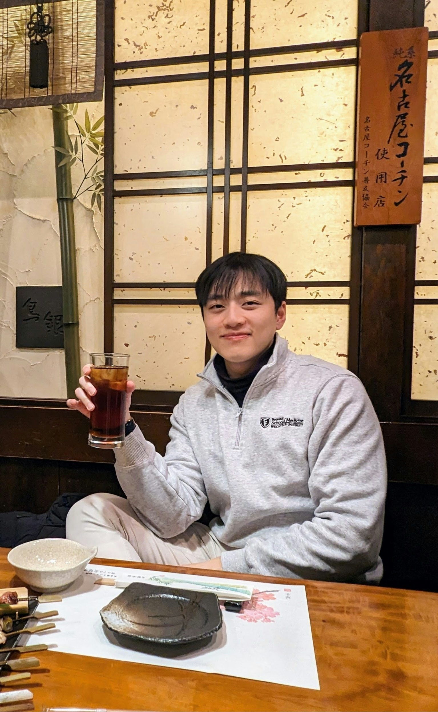 David Xiah posing with a drink in hand inside of a restaurant. 