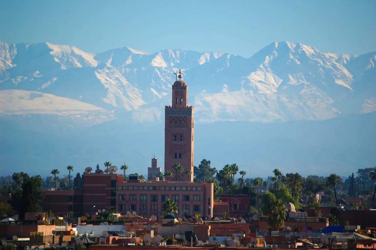 A view of the Atlas mountains from the Medina of Marrakech, with a prominent tower featured in the center